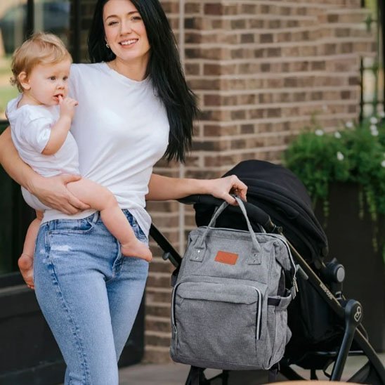 bébé dans le bras de maman et sac a langer accroché