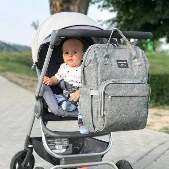 bébé dans la poussette et sac a langer gris accroché goudron arbres verdures
