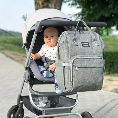 bébé dans la poussette et sac a langer gris accroché goudron arbres verdures